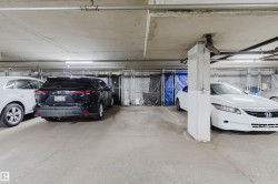 Underground parking garage featuring concrete flooring, exposed overhead piping, fluorescent lighting, and chain link storage units - 