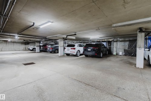 Concrete parking garage with exposed ceiling pipes and fluorescent lighting fixtures - 202 10939 82 Avenue, Edmonton, AB 