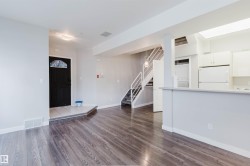 Open-concept living area featuring wood-finish flooring, a contemporary staircase with white railings, and a kitchen with white cabinetry and appliances - 