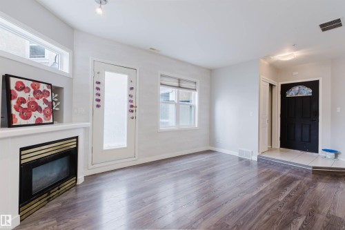 Spacious room featuring wood-finish flooring, a white mantel fireplace with a black and gold insert, and multiple windows for abundant light - 202 10939 82 Avenue, Edmonton, AB 