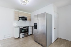 Kitchen featuring light wood-finish flooring, white subway tile backsplash, white cabinetry, and stainless steel appliances - 
