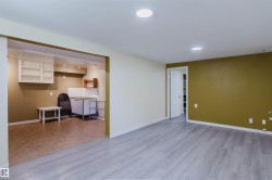 Open-concept room featuring wood-finish flooring, recessed lighting, and a doorway leading to an additional space with tiled flooring and wall-mounted shelving - 