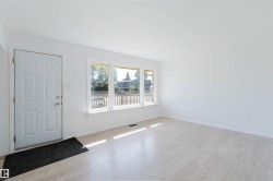 Bright interior space featuring a multi-pane window, wood-finish flooring, white walls, and a white entry door - 