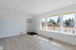 Open-concept living area with light wood-finish flooring, white walls, and a multi-pane picture window - 