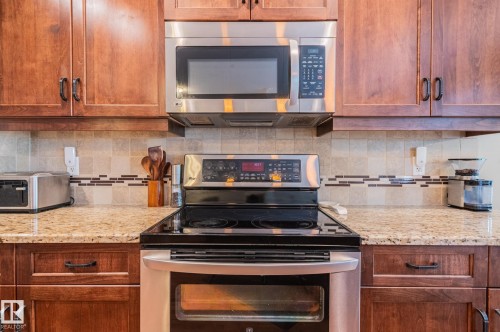 Kitchen featuring stainless steel appliances, rich wood cabinetry, patterned tile backsplash, and light-toned countertops - 19 Newton Place, St. Albert, AB - Indoor Photo Showing Kitchen
