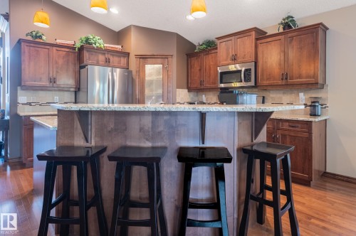 Kitchen featuring a large central island with seating, wood-finish flooring, full-height cabinetry, stainless steel appliances, and pendant lighting - 19 Newton Place, St. Albert, AB - Indoor Photo Showing Kitchen