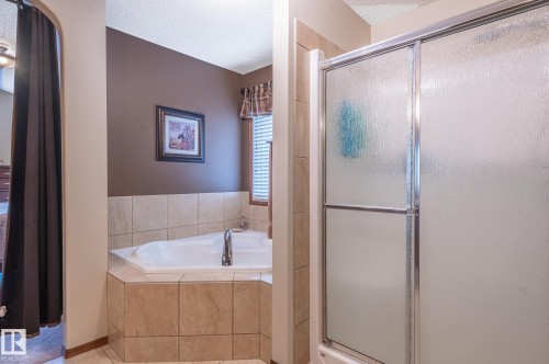 Tiled corner soaking tub with deck-mounted faucet and an enclosed shower with sliding frosted glass doors - 19 Newton Place, St. Albert, AB - Indoor Photo Showing Bathroom