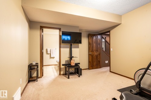 Carpeted room featuring a ceiling beam, recessed lighting, and a doorway to a tiled bathroom with a toilet and wall-mounted towel bar - 19 Newton Place, St. Albert, AB - Indoor Photo Showing Gym Room