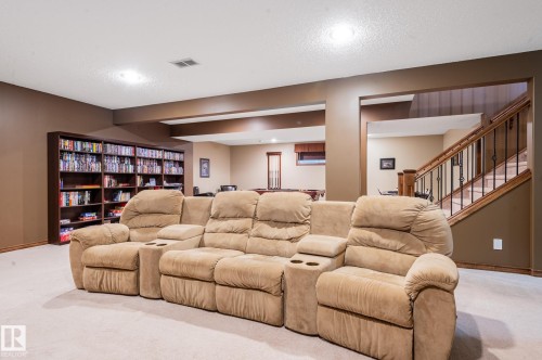 Carpeted lower level featuring recessed lighting, a full-wall built-in bookshelf, and a wood staircase with wrought iron balusters - 19 Newton Place, St. Albert, AB - Indoor Photo Showing Other Room