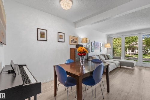 Open-concept living area with light wood-finish flooring, a contemporary overhead light fixture, and large windows providing abundant natural light - 10940 123 Street, Edmonton, AB 