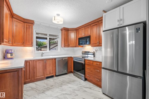 Kitchen featuring wood cabinetry, stainless steel appliances, white countertops, and a white tile backsplash - 10940 123 Street, Edmonton, AB 
