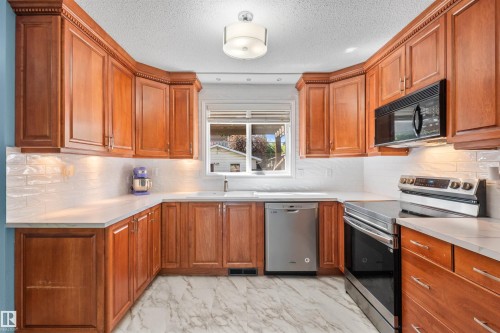 Kitchen featuring wood cabinetry with crown molding, white countertops, white subway tile backsplash, and light-tone flooring - 10940 123 Street, Edmonton, AB 