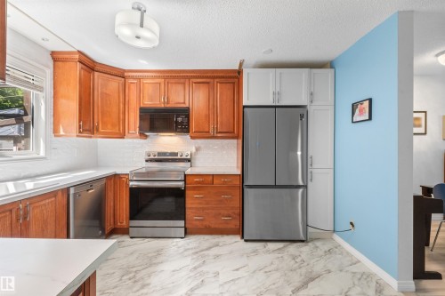 Kitchen featuring wood-finish cabinetry, stainless steel appliances, white subway tile backsplash, and stone-look flooring - 10940 123 Street, Edmonton, AB 