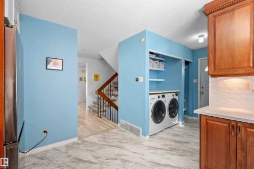 Integrated laundry station with storage shelving, adjacent to a kitchen area featuring wood cabinetry, light countertops, and a subway tile backsplash - 10940 123 Street, Edmonton, AB 