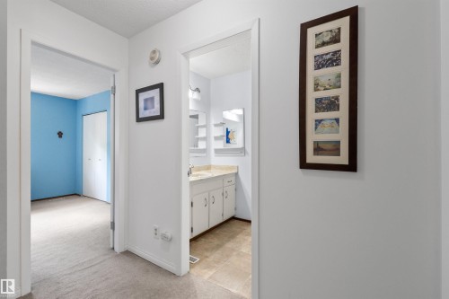 Hallway featuring neutral carpet flooring and white walls, leading to a room with blue walls and a closet with bifold doors - 10940 123 Street, Edmonton, AB 