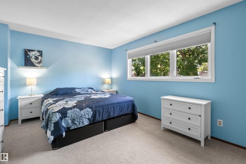 Light blue bedroom featuring a large window, white trim, and light-colored carpet flooring - 10940 123 Street, Edmonton, AB 