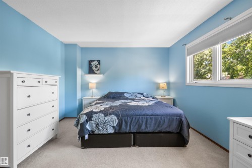 Bedroom featuring light blue walls, light-colored carpet flooring, and a large window with roller shades - 10940 123 Street, Edmonton, AB 