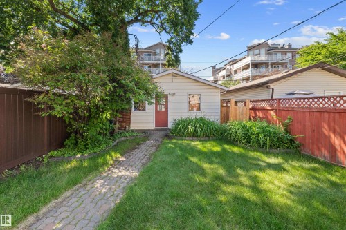 Rear exterior featuring a red door, white siding, and a stone paver path - 10940 123 Street, Edmonton, AB 