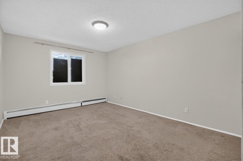 Carpeted room featuring light gray walls, a window with white trim, and baseboard heating units - 106 237 Woodvale Road W, Edmonton, AB 