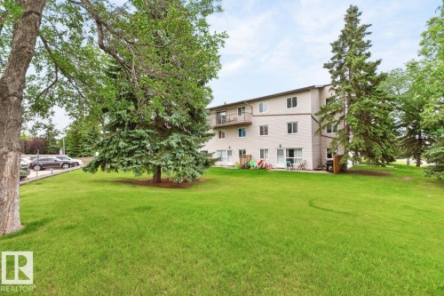 Expansive green space featuring a multi-story building, mature trees, and a paved parking area - 106 237 Woodvale Road W, Edmonton, AB 