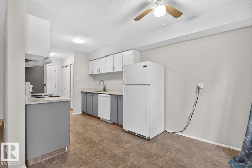 Kitchen featuring white upper cabinetry, grey lower cabinetry, a built-in dishwasher, and a stainless steel sink with a gooseneck faucet - 106 237 Woodvale Road W, Edmonton, AB 