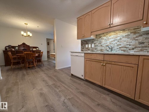 Kitchen area featuring light wood-finish cabinetry, a white dishwasher, stainless steel sink, and mosaic tile backsplash - 102 10903 21 Avenue, Edmonton, AB - Indoor Photo Showing Kitchen