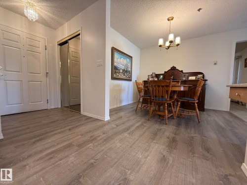 Entry foyer and dining area featuring wood-finish flooring, white paneled doors, mirrored closet doors, a crystal chandelier, and a brass-finished dining chandelier - 102 10903 21 Avenue, Edmonton, AB - Indoor Photo Showing Dining Room