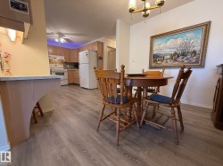 Open-concept living space featuring wood-finish flooring, a kitchen with light wood cabinetry and white appliances, and a dining area - 