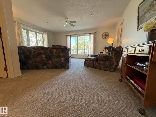 Bright living space featuring a ceiling fan, light-toned carpeting, and a built-in wall heater - 102 10903 21 Avenue, Edmonton, AB - Indoor Photo Showing Living Room
