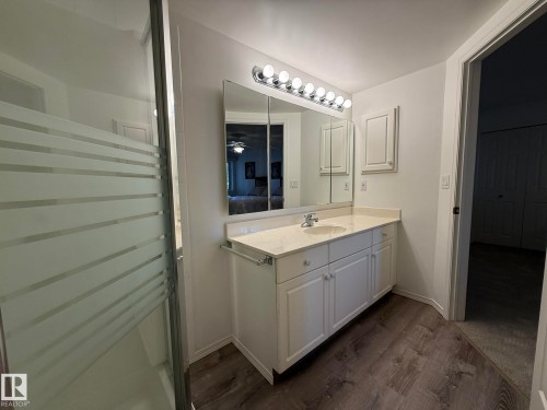 Bathroom vanity featuring a single basin sink, light-toned countertop, and white cabinetry - 102 10903 21 Avenue, Edmonton, AB - Indoor Photo Showing Bathroom