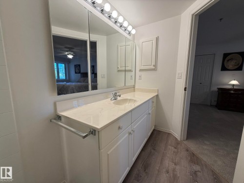 White vanity with a single basin sink, white countertop, and matching wall cabinet - 102 10903 21 Avenue, Edmonton, AB - Indoor Photo Showing Bathroom