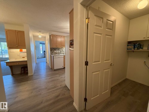 Interior hallway featuring wood-finish flooring, a built-in desk area with upper cabinetry, a kitchen area with light wood cabinetry and a tile backsplash, and a utility space with a shelf and upper cabinetry - 102 10903 21 Avenue, Edmonton, AB - Indoor