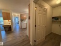 Interior hallway featuring wood-finish flooring, a built-in desk area with upper cabinetry, a kitchen area with light wood cabinetry and a tile backsplash, and a utility space with a shelf and upper cabinetry - 102 10903 21 Avenue, Edmonton, AB  - Indoor 