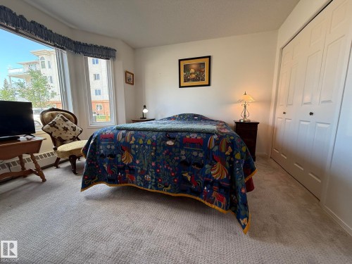 Carpeted room featuring a large bay window, white walls, and white bi-fold closet doors - 102 10903 21 Avenue, Edmonton, AB - Indoor Photo Showing Bedroom