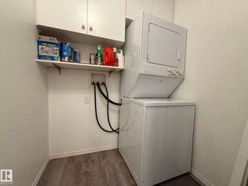 Laundry area featuring a stackable washer and dryer, wood-finish flooring, and white cabinetry with a built-in shelf - 102 10903 21 Avenue, Edmonton, AB - Indoor Photo Showing Laundry Room