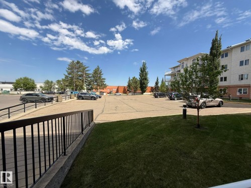 Expansive outdoor parking area featuring paved surfacing, mature trees, and a low-rise residential building in the background - 102 10903 21 Avenue, Edmonton, AB - Outdoor