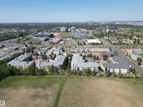 Expansive aerial perspective showcasing the surrounding neighborhood, featuring multi-story residential buildings, commercial structures, and a prominent green space - 102 10903 21 Avenue, Edmonton, AB - Outdoor With View