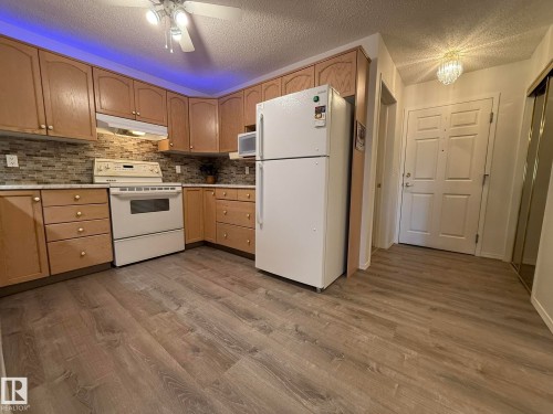 Kitchen featuring wood cabinetry, white appliances, mosaic tile backsplash, solid surface countertops, and wood-finish flooring - 102 10903 21 Avenue, Edmonton, AB - Indoor Photo Showing Kitchen