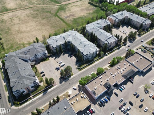 Aerial overview of a multi-building complex featuring grey shingle roofs, exterior balconies, and surrounding mature trees - 102 10903 21 Avenue, Edmonton, AB - Outdoor With View