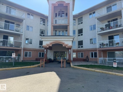 Multi-story stucco building with individual balconies featuring white railings, a prominent entrance portico with an arched detail, and multiple window configurations - 102 10903 21 Avenue, Edmonton, AB - Outdoor With Facade