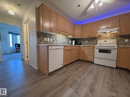Kitchen featuring wood-finish cabinetry, white appliances, a mosaic tile backsplash, and light-toned countertops - 102 10903 21 Avenue, Edmonton, AB - Indoor Photo Showing Kitchen