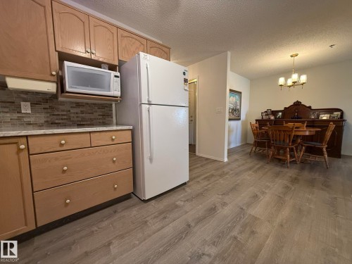 Kitchen area featuring light wood cabinetry, a mosaic tile backsplash, and a white refrigerator - 102 10903 21 Avenue, Edmonton, AB - Indoor Photo Showing Kitchen