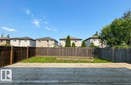 Expansive outdoor wood deck with a natural finish, bordering a fenced yard featuring a grassy area and a raised garden bed - 1919 Hammond Place, Edmonton, AB 