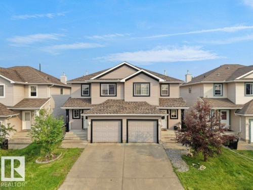 Two-story duplex featuring neutral siding with dark trim accents, a two-car attached garage, and a concrete driveway - 8111 7 Avenue Sw, Edmonton, AB 