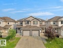 Two-story duplex featuring neutral siding with dark trim accents, a two-car attached garage, and a concrete driveway - 8111 7 Avenue Sw, Edmonton, AB 