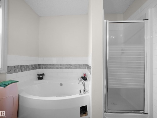 Corner soaking tub with polished chrome fixtures and a tiled surround featuring a decorative accent band - 8111 7 Avenue Sw, Edmonton, AB 