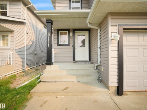 Front facade featuring neutral horizontal siding, a white entry door with glass paneling, and an attached garage with a panel-style door - 8111 7 Avenue Sw, Edmonton, AB 