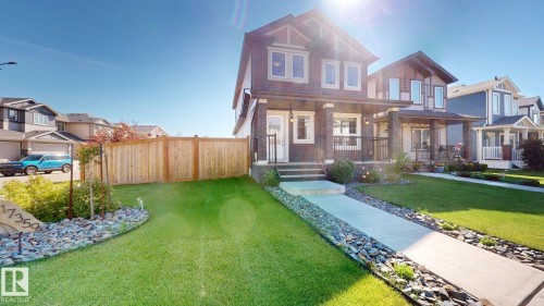 Two-story residence featuring a dark siding facade with white trim, a covered front porch, and a manicured front lawn - 17359 49 Street, Edmonton, AB 