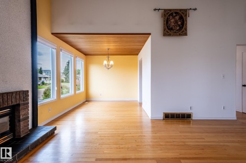 Spacious interior featuring wood-finish flooring, a brick fireplace with a black tile hearth, and a row of three large windows - 11415 142 Avenue, Edmonton, AB 
