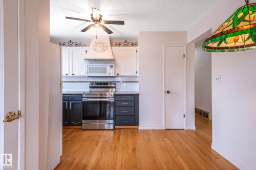 Kitchen featuring wood-finish flooring, two-tone cabinetry, stainless steel appliances, and a decorative range hood - 11415 142 Avenue, Edmonton, AB 